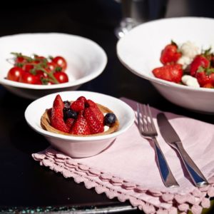 Strawberries and fresh fruit in white bowls with pink napkins